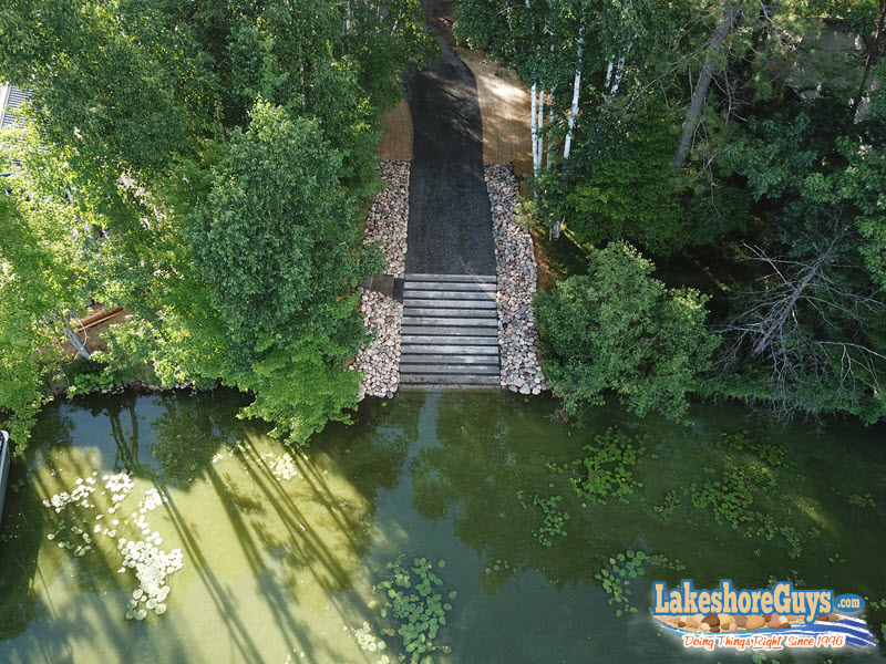 Segmented concrete boat ramp with long gravel path, riprap shoreline, and staircase - aerial view